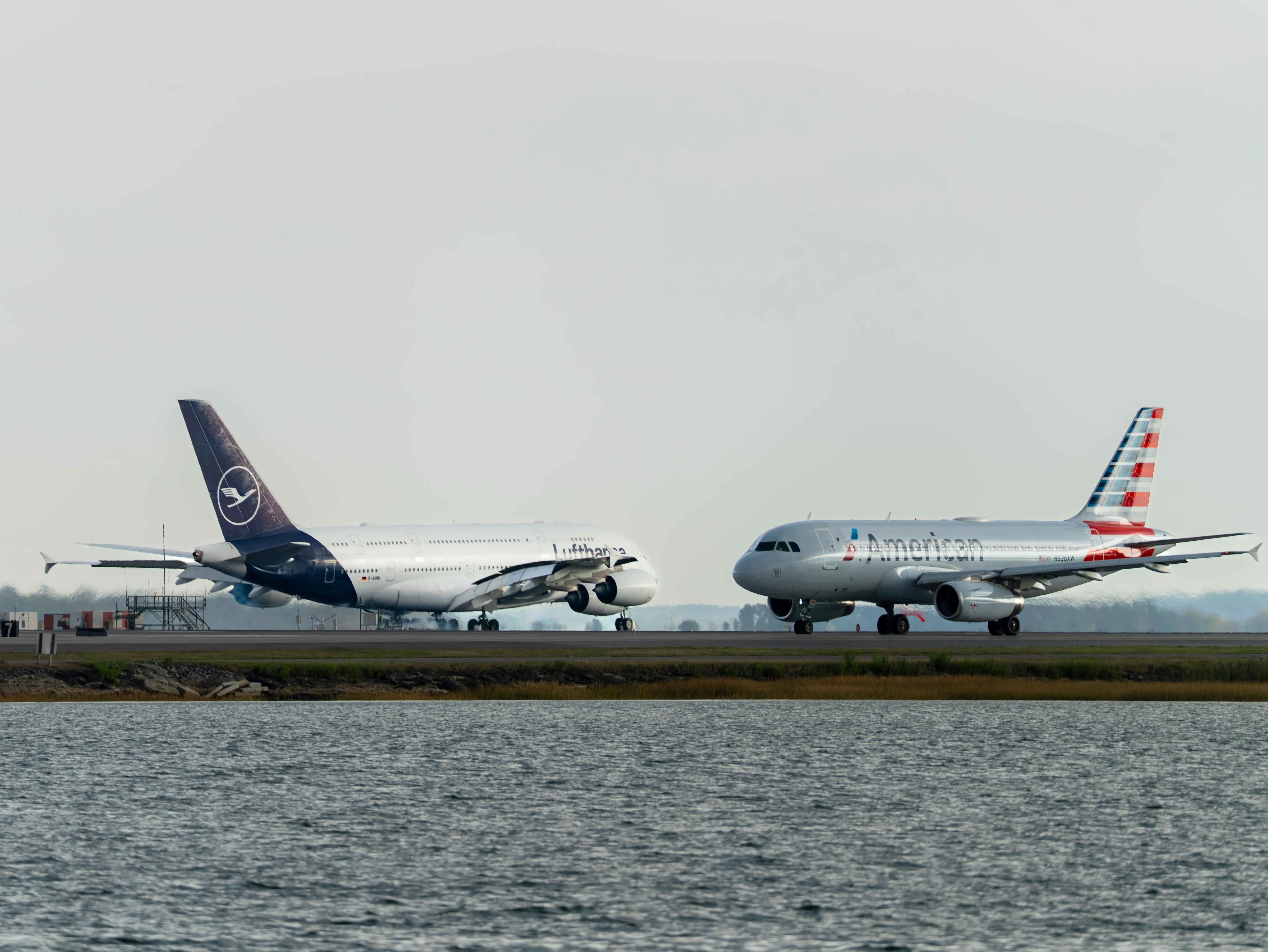 Lufthansa Airbus A380-841 (registration number D-AIMB) and American Airlines Airbus A319-132 (registration number N826AW) appear to be the same size due to perspective, as the closer A319 makes the farther A380 look smaller