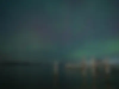 Aurora in the sky with a small port nearby and lights in the distance