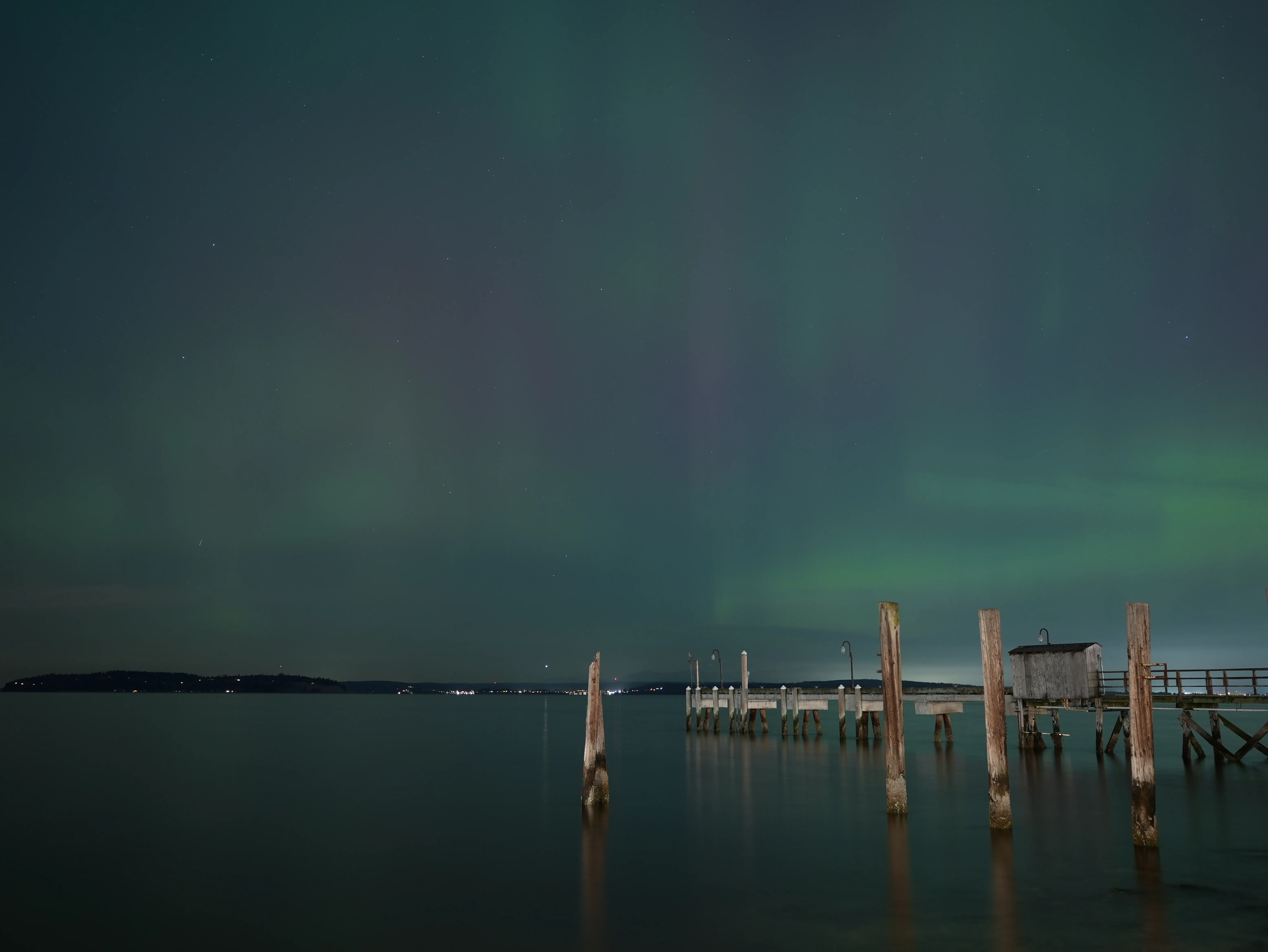 Aurora in the sky with a small port nearby and lights in the distance